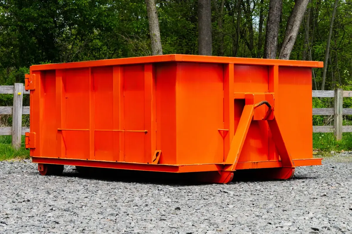 Orange roll-off dumpster parked on a gravel lot