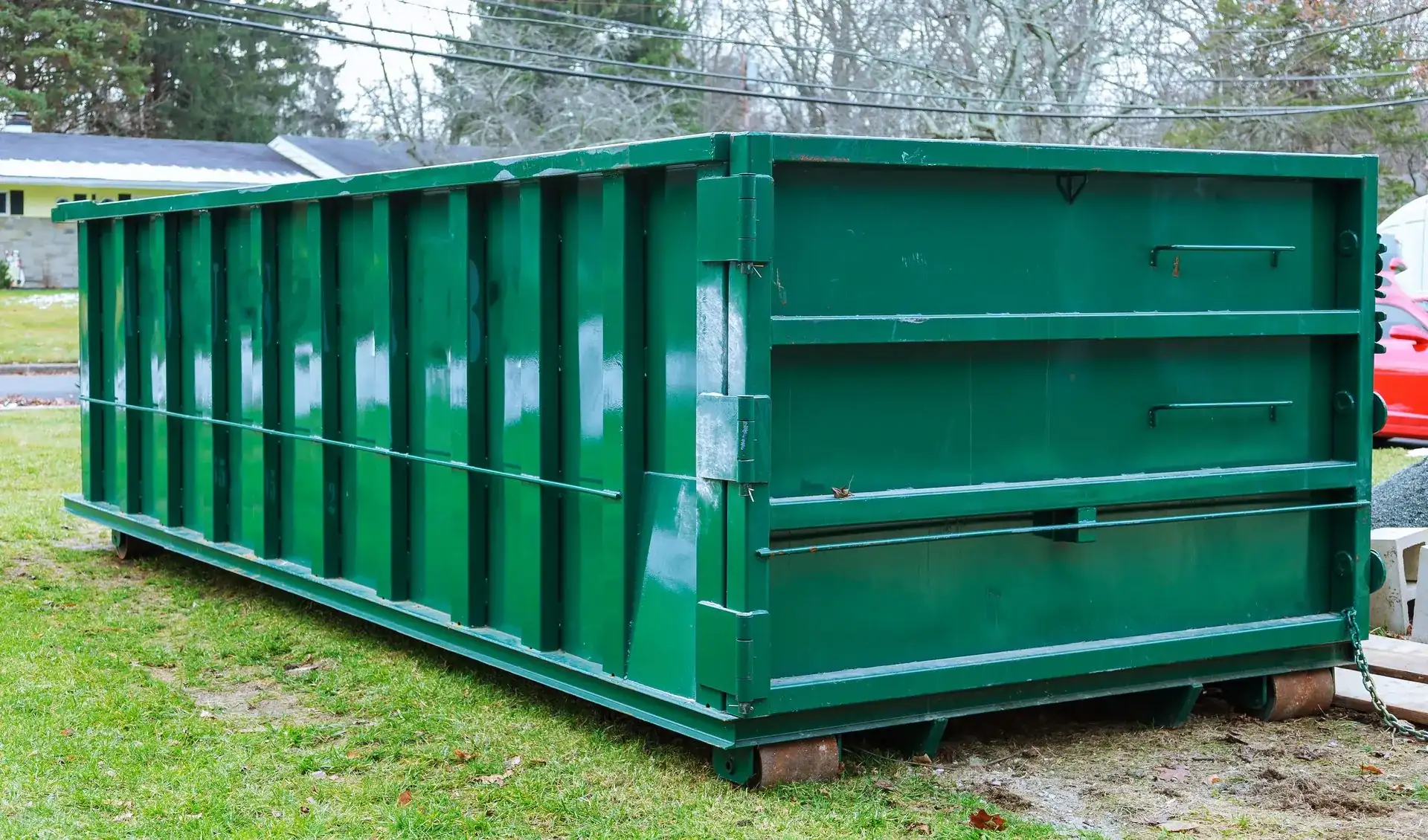 Green roll-off dumpster set on wood boards beside a house